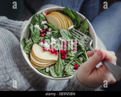 Donna in jeans e maglione holding vegane insalatiera con spinaci, pera, melograno, formaggio. Colazione Vegana Vegetariana Cibo, dieta concetto. La ragazza di j Foto Stock