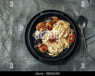 Polpette Pasta Carbonara in piatto nero artigianale su sfondo grigio. Vista ravvicinata della carbonara cremosa con spazio per le copie. Concetto di cibo confortevole. Vista dall'alto Foto Stock