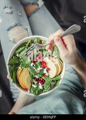 Donna in jeans azienda vegan insalatiera con spinaci, pera, melograno, formaggio. Colazione Vegana Vegetariana Cibo, dieta concetto. Ragazza in jeans azienda Foto Stock