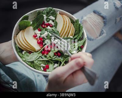 Donna in jeans azienda vegan insalatiera con spinaci, pera, melograno, formaggio. Colazione Vegana Vegetariana Cibo, dieta concetto. Ragazza in jeans azienda Foto Stock