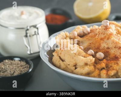 In casa hummus con olio di oliva in grigio ciotola e ingredienti. Tradizionali del medio oriente hummus antipasto su sfondo grigio - sano pasta vegano snac Foto Stock