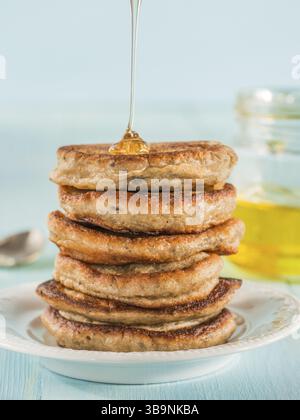 Pila di piccole pancake con banana e semi di chia nel miele su fondo azzurro. Il miele di versarla sulla pila di mini pancake con chia o di papavero, vedere Foto Stock