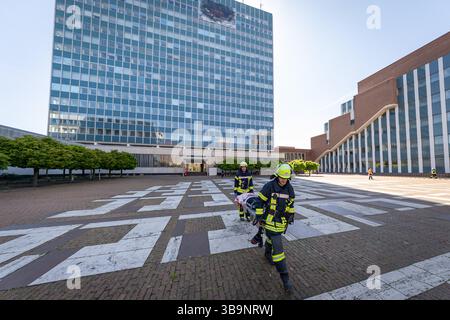 10 maggio 2025, Baviera, Erlangen: I servizi di emergenza salvano i feriti (extra) da un edificio in cui un aereo si è schiantato come parte dell'esercitazione di controllo del disastro "Löwenzahn" - nella foto su un telone sulle file superiori delle finestre. Nello scenario di esercitazione, un aereo cargo si è schiantato sopra il centro della città. Parti di un alto edificio sono state gravemente danneggiate. I piani superiori di un edificio di uffici adiacente sono in fiamme. E in un impianto chimico fittizio nelle vicinanze, la coda dell'aereo schiantata ha danneggiato diversi contenitori con merci pericolose. La stessa cabina di pilotaggio dell'aereo si è schiantata su un'auto all'en Foto Stock