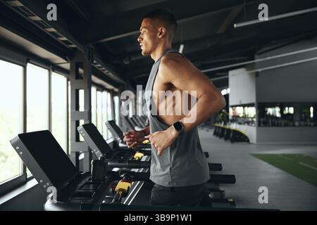Side shot di un atleta con abbigliamento sportivo che corre sul tapis roulant nella moderna palestra Foto Stock