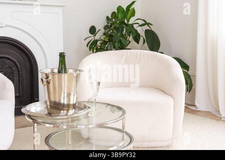 Elegante soggiorno con secchiello di ghiaccio metallico che contiene champagne. Due eleganti bicchieri sono seduti su un tavolo di vetro, pronti per un'occasione di festa in stile moderno Foto Stock