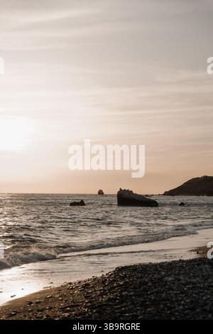 Tramonto sul mare con rocce in acqua e dolci onde che bagnano la riva, atmosfera tranquilla e tranquilla. Foto Stock