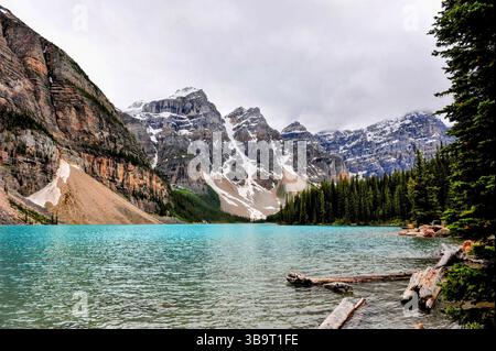 Le acque turchesi del lago Moraine riflettono aspre cime innevate e fitte foreste di pini, creando uno splendido paesaggio delle Montagne Rocciose canadesi. Foto Stock
