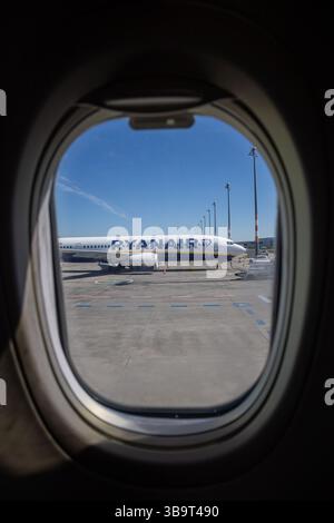 Berlino, Germania, 28.4,2025: Una vista dalla finestra di un aereo mostra un aereo Ryanair parcheggiato sull'asfalto sotto un cielo azzurro. Le caratteristiche dell'aeromobile Foto Stock