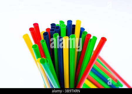 Primo piano di vibranti cannucce in plastica in una tazza gialla su sfondo bianco minimalista. Foto Stock