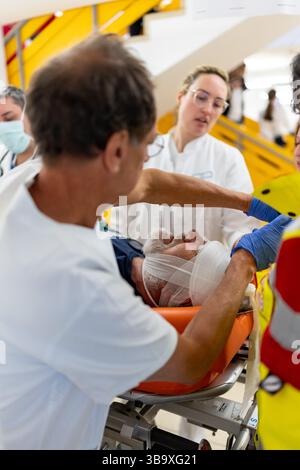 10 maggio 2025, Baviera, Erlangen: I dipendenti dell'ospedale universitario di Erlangen assistono una persona ferita (extra) nel reparto di triage del pronto soccorso nell'ambito dell'esercizio di controllo delle catastrofi "Löwenzahn". Nello scenario di esercitazione, un aereo cargo si è schiantato sopra il centro della città. Parti di un alto edificio sono state gravemente danneggiate. I piani superiori di un edificio di uffici adiacente sono in fiamme. E in un impianto chimico fittizio nelle vicinanze, la coda dell'aereo schiantata ha danneggiato diversi contenitori con merci pericolose. La cabina di pilotaggio dell'aereo si è schiantata su un'auto all'ingresso di un parcheggio sotterraneo Foto Stock