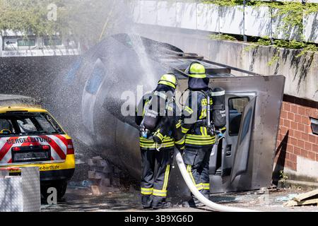 10 maggio 2025, Baviera, Erlangen: I vigili del fuoco stanno lavorando su un cockpit (modello) di aerei che si è schiantato in un vialetto di parcheggio sotterraneo come parte dell'esercitazione di controllo delle catastrofi "Löwenzahn". Nello scenario di esercitazione, un aereo cargo si è schiantato sopra il centro della città. Parti di un alto edificio sono state gravemente danneggiate. I piani superiori di un edificio di uffici adiacente sono in fiamme. E in un impianto chimico fittizio nelle vicinanze, la coda dell'aereo schiantata ha danneggiato diversi contenitori con merci pericolose. La cabina di pilotaggio dell'aereo si è schiantata su un'auto all'ingresso di un parcheggio sotterraneo Foto Stock