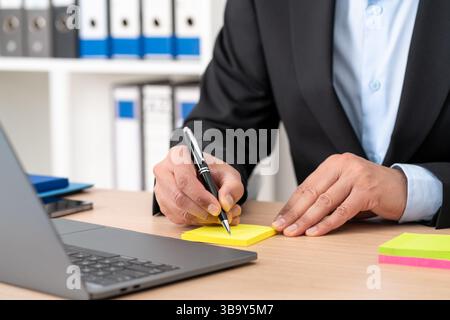 Primo piano di un uomo d'affari che scrive a mano su una nota postale in ufficio Foto Stock