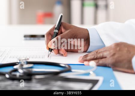 Primo piano di mani del medico che scrivono su carta o documento a un desktop in ospedale.professionista sanitario redazione di una lettera di assicurazione medica, legale Foto Stock