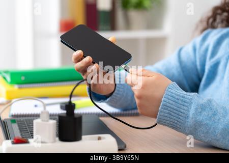 Primo piano di una donna d'affari che collega il cavo di ricarica a uno smartphone di casa Foto Stock