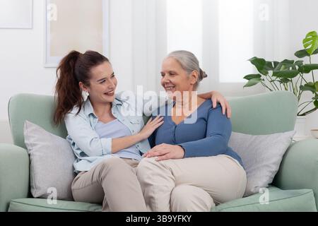 La nipote abbraccia la nonna sorridente con amore e gioia. Momenti familiari caldi e felici a casa mostrando affetto, connessione e generazionale Foto Stock