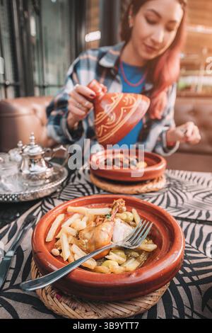 Donna che apre una tajine in ceramica per mangiare un tradizionale stufato di pollo marocchino in un ristorante Foto Stock