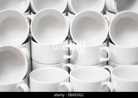 Tazze da caffè in ceramica bianca impilate in file. Schema ripetitivo di tazze pulite vuote. Sfondo dal design minimalista. Utensili da cucina moderni o attrezzature da caffè Foto Stock