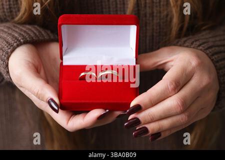 Donna che tiene la scatola ad anello. Portagioie in velluto rosso. Fidanzamento o fede nuziale. Idea regalo romantica. Mani che presentano il simbolo del matrimonio. Foto Stock