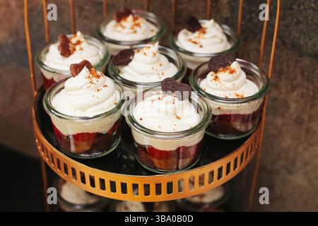Dessert in vasetti di vetro. Panna montata sopra. Dolcetti a strati. Dolci per feste a buffet. Mousse o gelatina fatte in casa. Elegante presentazione in piccole porzioni. Foto Stock