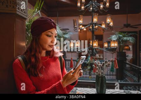 Giovane donna che indossa un turbante usando il telefono cellulare nel cortile di un riad tradizionale marocchino a Marrakech Foto Stock