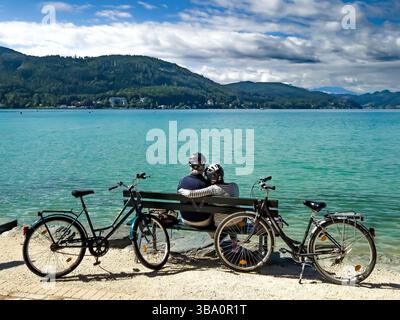 Una coppia Senior sportiva con biciclette siede sulla panchina del lago Woerthersee in Carinzia, Austria Foto Stock