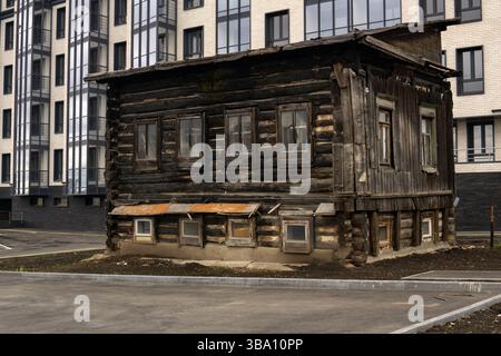 vecchia casa in legno sullo sfondo di un edificio moderno a più piani di nuova costruzione Foto Stock