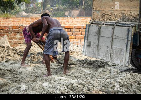 Due uomini che usano le pale per spostare la sabbia da un cantiere vicino a un autocarro Foto Stock