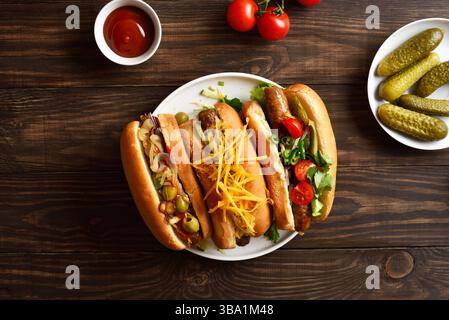 Hot dog con diverse guarnizioni su piatto bianco su sfondo di legno. Vista dall'alto, disposizione piatta Foto Stock