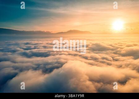 Vista aerea dell'alba dorata sul mare di nebbia e paesaggio montano Foto Stock