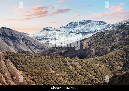 Splendido panorama delle innevate montagne dell'Atlante che brillano di arancione durante il tramonto in Marocco, mostrando la bellezza unica della natura nordafricana Foto Stock