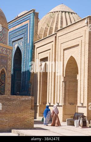 Due donne in abito tradizionale camminano accanto agli ingressi ad arco ai mausolei della Necropoli Shah-i-Zinda, Samarcanda, Uzbekistan Foto Stock