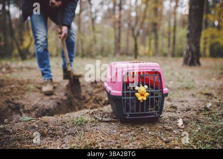 Scena Spooky al cimitero degli animali domestici. La tomba di amici animali perduti. Compagnia, addio. Un uomo porta un animale domestico morto in un vettore alla foresta e di Foto Stock