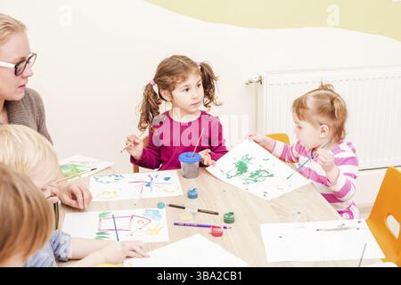 I bambini e i tutor sono la verniciatura con un pennello e acquerelli su carta nella scuola materna Foto Stock