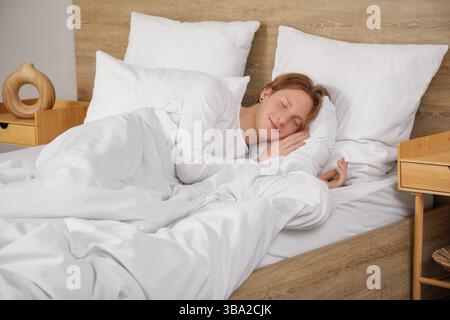 Bel giovane uomo felice in pigiama con cuscini che dormono sul letto a casa Foto Stock