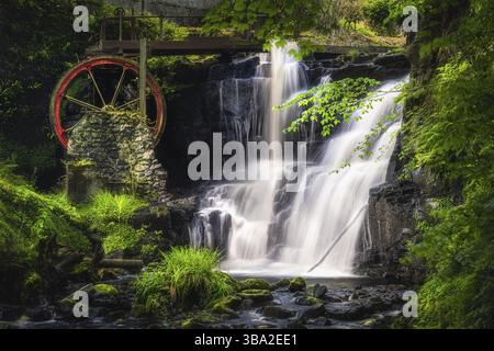 Ruota d'acqua rossa d'epoca con cascata in primavera nel Glenareff Forest Park, County Antrim, Irlanda del Nord. Foto a lunga esposizione e messa a fuoco morbida Foto Stock