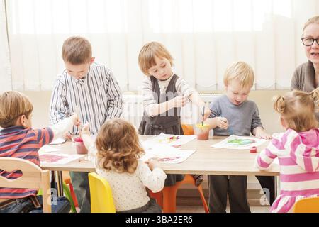 I bambini e i tutor sono la verniciatura con un pennello e acquerelli su carta nella scuola materna Foto Stock