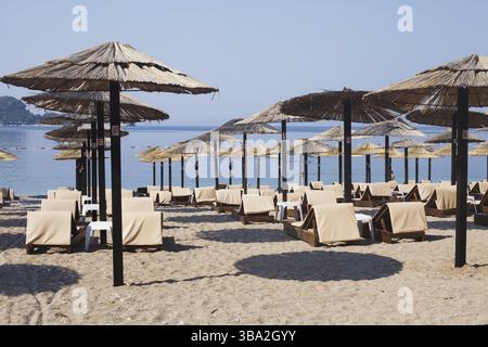 File di sedie a sdraio in legno marrone e ombrelloni in paglia sulla spiaggia di mare al mattino. Budva, Montenegro, Europa Foto Stock