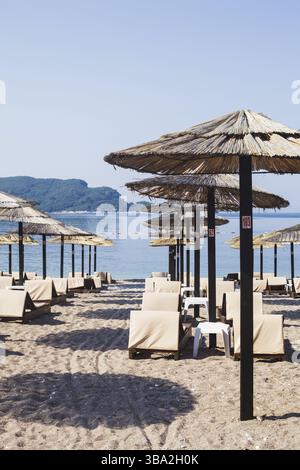 File di sedie a sdraio in legno marrone e ombrelloni in paglia sulla spiaggia di mare al mattino. Budva, Montenegro, Europa Foto Stock