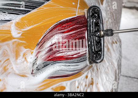 Pennello lasciando le pennellate in sapone e schiuma di auto gialla lavata in autolavaggio Foto Stock