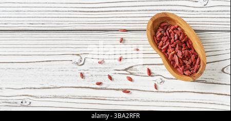 goji essiccato alias. Semi di wolfberry in una ciotola di legno e versati sulla scrivania delle lavagne bianche vicino, vista dall'alto, Liptovsky Mikulas, Slovacchia, Europa Foto Stock