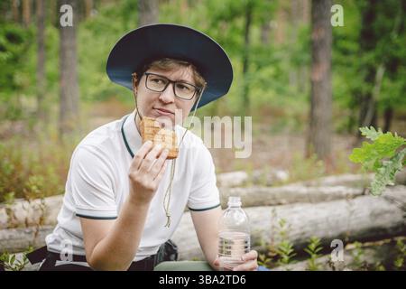 Femmina escursionista mangiare sandwich in natura. Donna turistica che fa colazione o pranzo al picnic, che mangia panini caldi mentre trascorre del tempo in natura. Viaggio Foto Stock