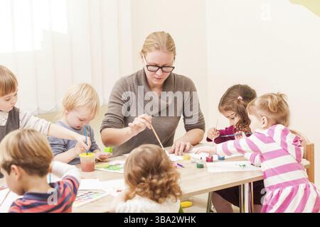 I bambini e i tutor sono la verniciatura con un pennello e acquerelli su carta nella scuola materna Foto Stock