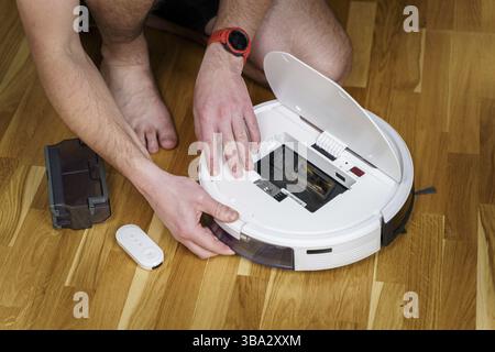 Concetto di casalinghi e tecnologia. Manutenzione ed assistenza di aspirapolvere robot. Pulizia, riparazione, sostituzione delle parti. Uomo che ripara il pulitore robot Foto Stock