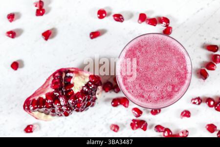 Frullato di melograno con frutti come gemme sfocati sparsi vicino sulla lavagna bianca. Foto dall'alto, concentrati sulle bolle nella schiuma per bevande, Liptovsky Hradok, S. Foto Stock