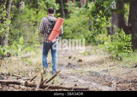 Concedi un viaggio e un'avventura mozzafiato. Escursione con vista sul retro, coraggioso ragazzo caucasico con passeggiate con zaino nella foresta lungo la strada di campagna. Turismo a tema e altro Foto Stock