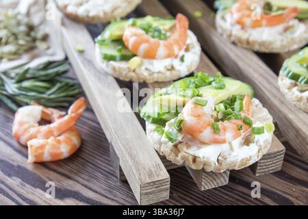 Torte di riso con fette di avocado cetrioli gamberi e formaggio spalmabile. Prezzemolo fresco e rosmarino. Concetto vegetariano e vegano. Profondità di campo ridotta. Colori Foto Stock