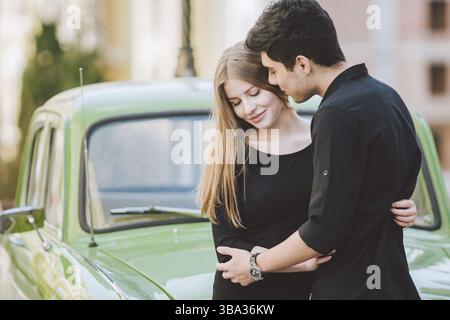 Giovani multirazziale giovane maschio e femmina amanti persone eterosessuali gli studenti. I bellissimi modelli in posa in piedi vicino a un retrò auto in città. Vestito Foto Stock