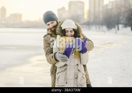 Una giovane coppia allegramente galleggia nella neve. Tra una lotta comica. Felice giovane coppia abbraccia nei boschi innevati invernali. Stile di vita romantico uomini e donne in lov Foto Stock