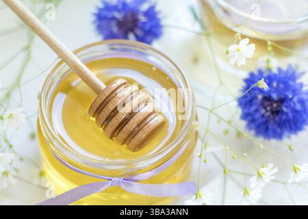 Miele in vasetti di vetro e tazza di tè con fiori bianchi primaverili e fiordaliso su davanzale. Profondità di campo ridotta Foto Stock