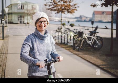 Una donna ha noleggiato uno scooter elettrico e ha intenzione di andare in una giornata invernale di sole in Danimarca, Copenaghen. Tema di trasporto ecologico e pulito. Nuovo qui Foto Stock